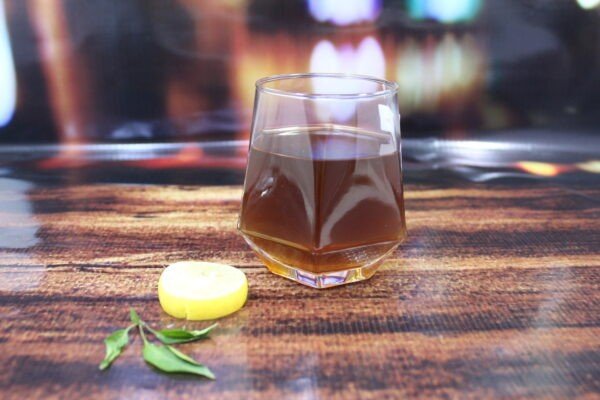 Transparent whisky glass with lemon slice and leaf on decorative background