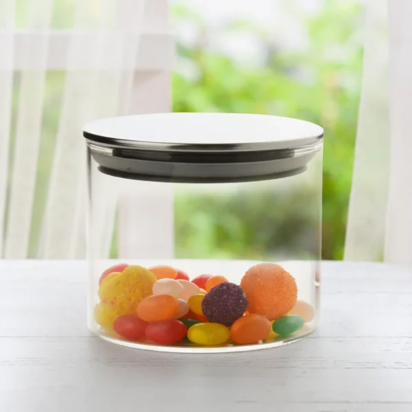 Transparent round glass container with steel lid filled with candy on white background