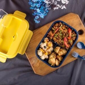 Three compartment leakproof lunch box filled with food, lunch on wooden chopping board on decorative background