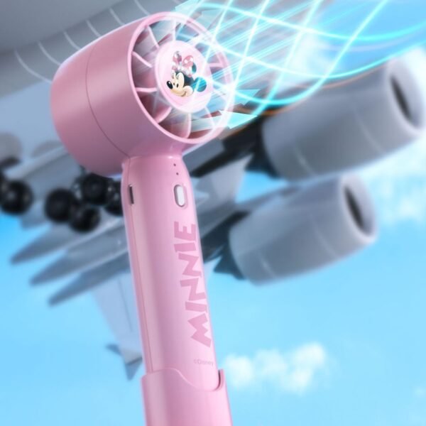 A pink handheld fan with Minnie Mouse on it. The fan is blowing air and there is an airplane in the background.