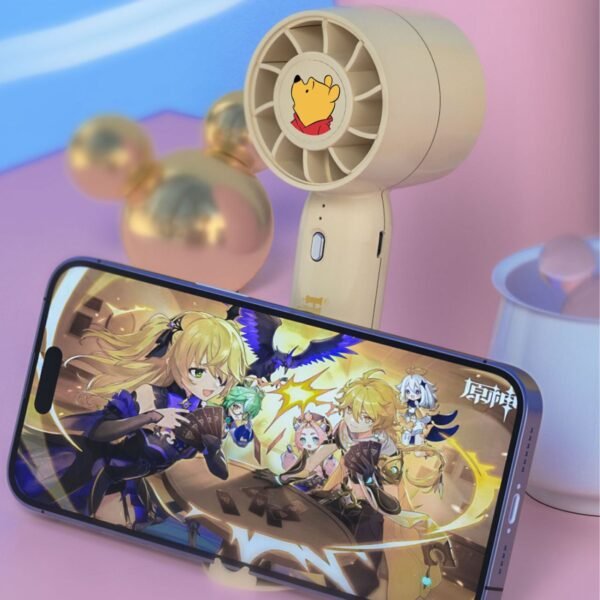 A beige handheld fan with Winnie the Pooh on it is cooling down a smartphone. The phone is displaying a video game with characters from the game Genshin Impact