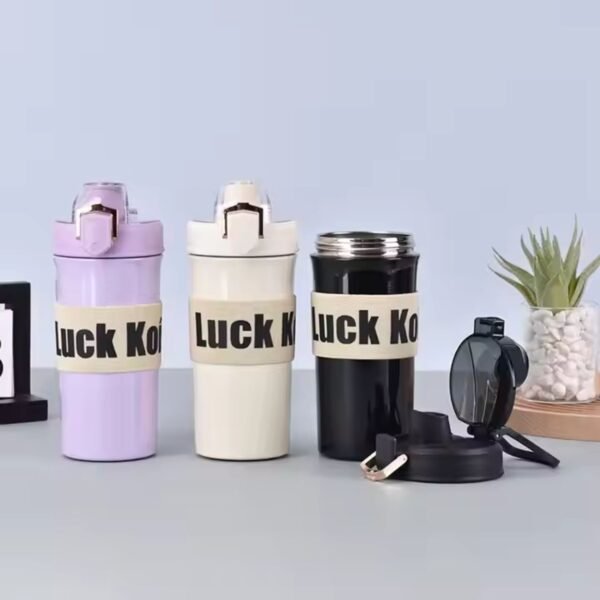 Three stylish tumbler bottles in lavender, white and black with the text "Luck Koi" printed on a strap, displayed on a minimalist table setting with a plant in the background.