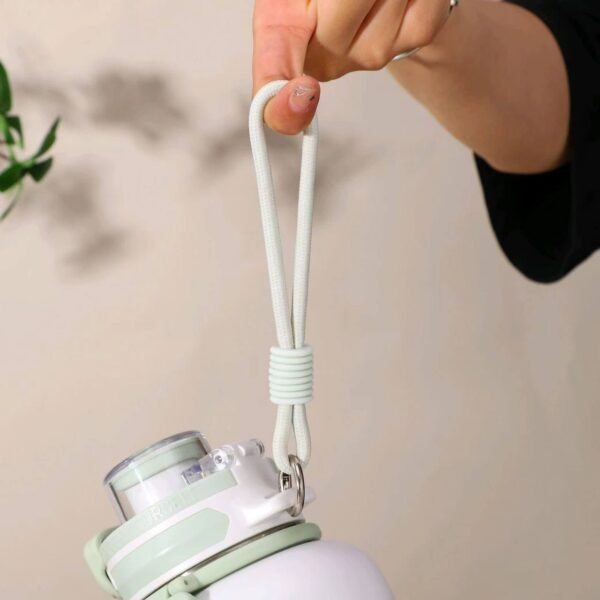 A hand holding a white and mint green water bottle by its durable light green silicone carry strap, highlighting the bottle's portability and comfortable grip.