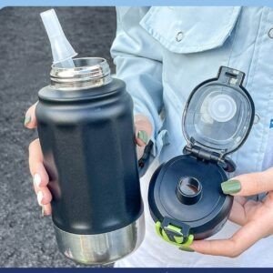 A person holding a black stainless steel water bottle with a straw lid. The lid is open, revealing a straw and a clear plastic cap