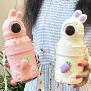 A girl holding two children's water bottle sipper shaped like rabbits. The pink bottle has a carrot attached and the white bottle has a purple carrot attached. Both bottles have straps with LED Temperature display and the word 'RABBIT' printed on them.