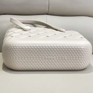 Beige perforated tote bag with a single handle, white button accent, and studded pattern on sofa