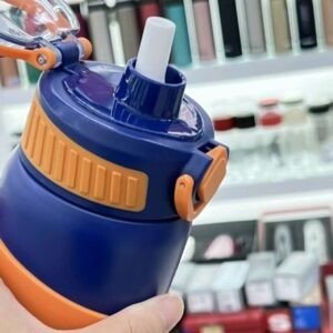 Close-up of a blue and orange water bottle with a straw, held in a hand, with a blurry store background