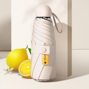 Compact white travel umbrella with UPF 50+ UV protection, shown closed next to a lemon.