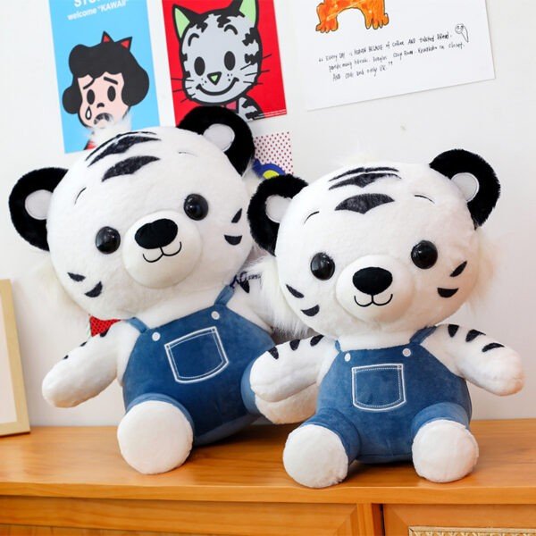 Pair of white tiger plush toys with black stripes and matching blue denim overalls sitting on a wooden surface