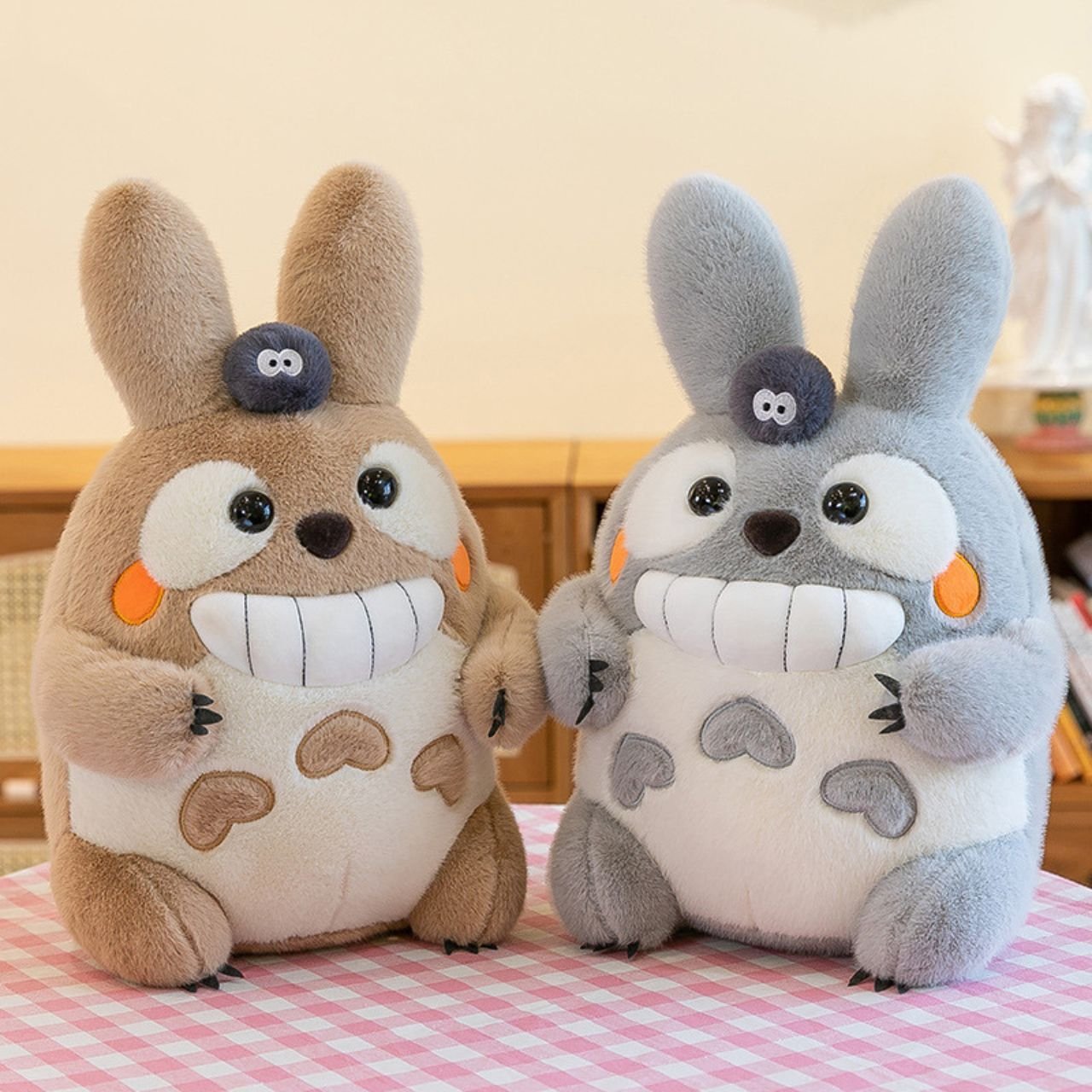 Pair of large, smiling plush rabbit toys, one brown and one grey, each featuring a black soot sprite on its head; wholesale bulk stuffed animal set.