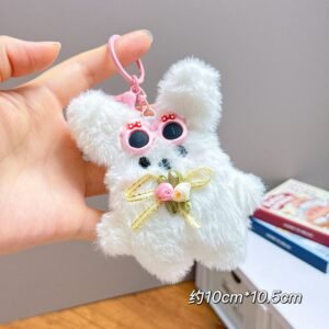 Hand holding a cute bunny plush toy keyring with metal clasp on decorative background.