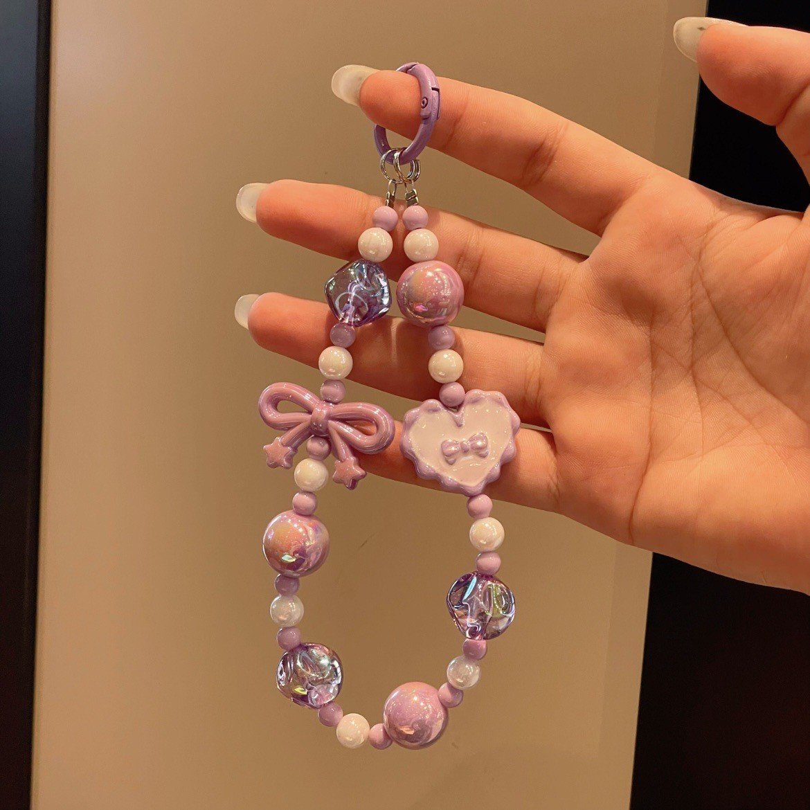 Hand holding a pastel acrylic beaded mobile phone charm with heart and start accents to show slcale.