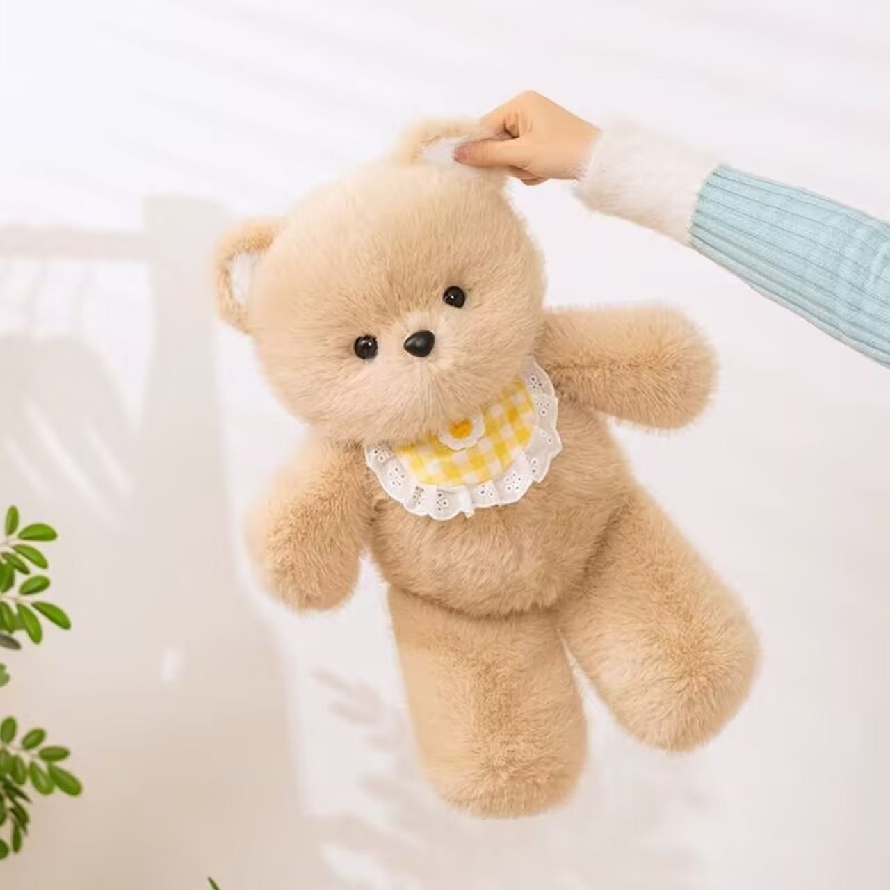 Person holding a large light brown teddy bear plush toy wearing a yellow checkered bib